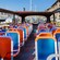 A tour bus with an open top parked next to a small seaside port filled with sail boats